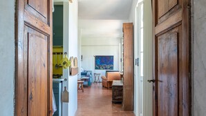 A narrow hallway with wooden doors, a kitchen area, a dining table, and a blue painting on the wall. - The sea in a room (Lerici SP)