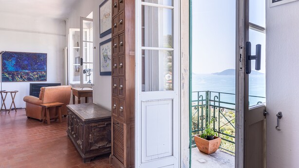 A room with a wooden cabinet, a chair, a small table, and a view of the sea through a balcony door. - The sea in a room (Lerici SP)
