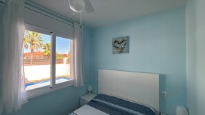 Ein Schlafzimmer mit einem Bett, einem Fenster mit Vorhängen, einem Deckenventilator und einem Wandbild.
