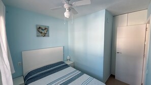A bedroom with a single bed, a ceiling fan, a nightstand, and a door.