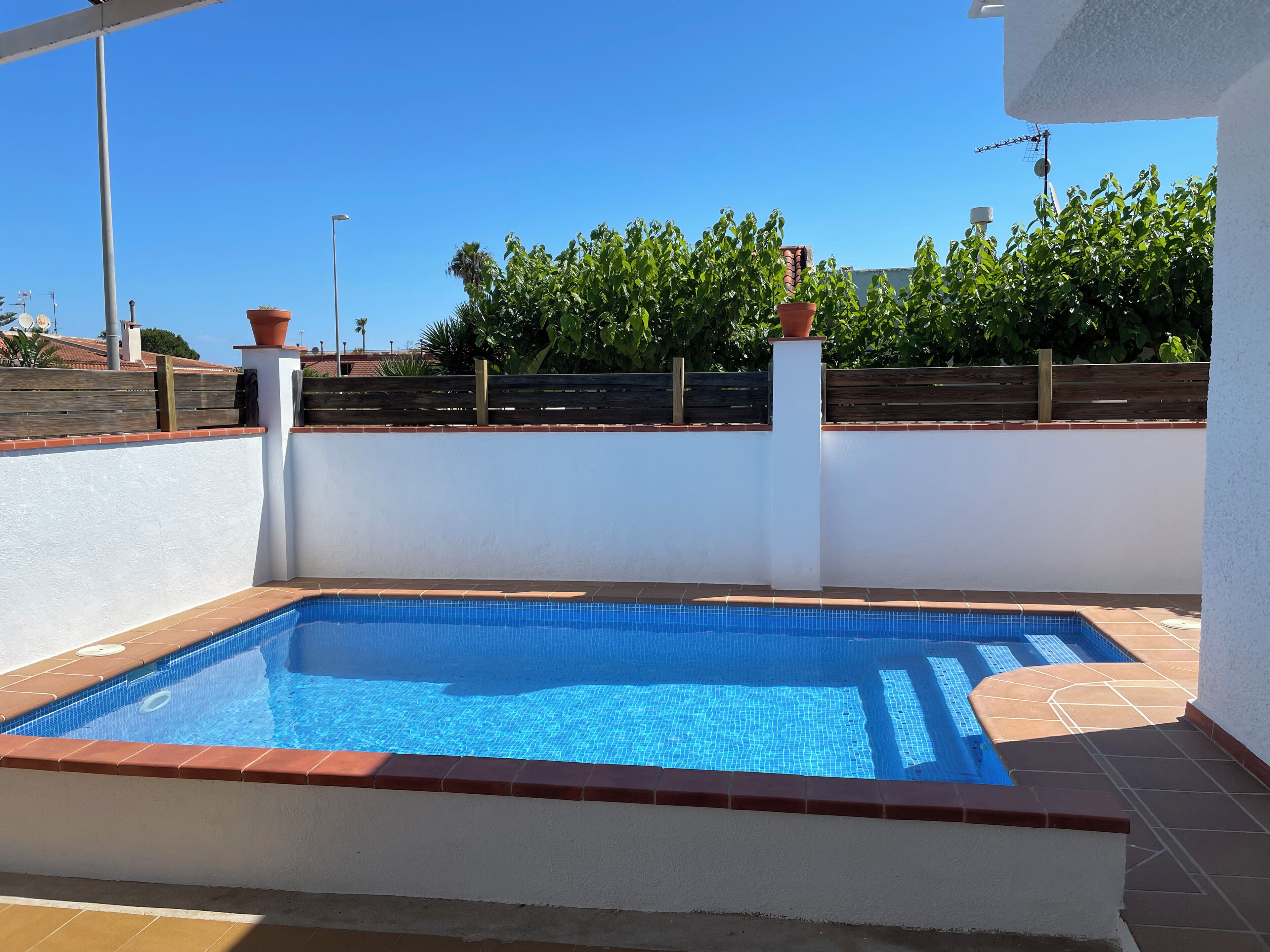 A rectangular swimming pool with a tiled edge, surrounded by a white wall and a wooden fence.