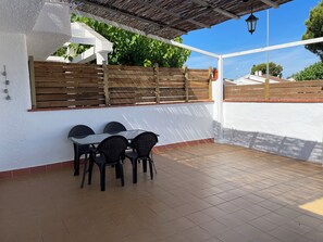 A patio with a table and chairs, a wooden fence, and a white wall. - Casa Rogi, with pool, ideal for family, on main street and near the beach (Riumar)