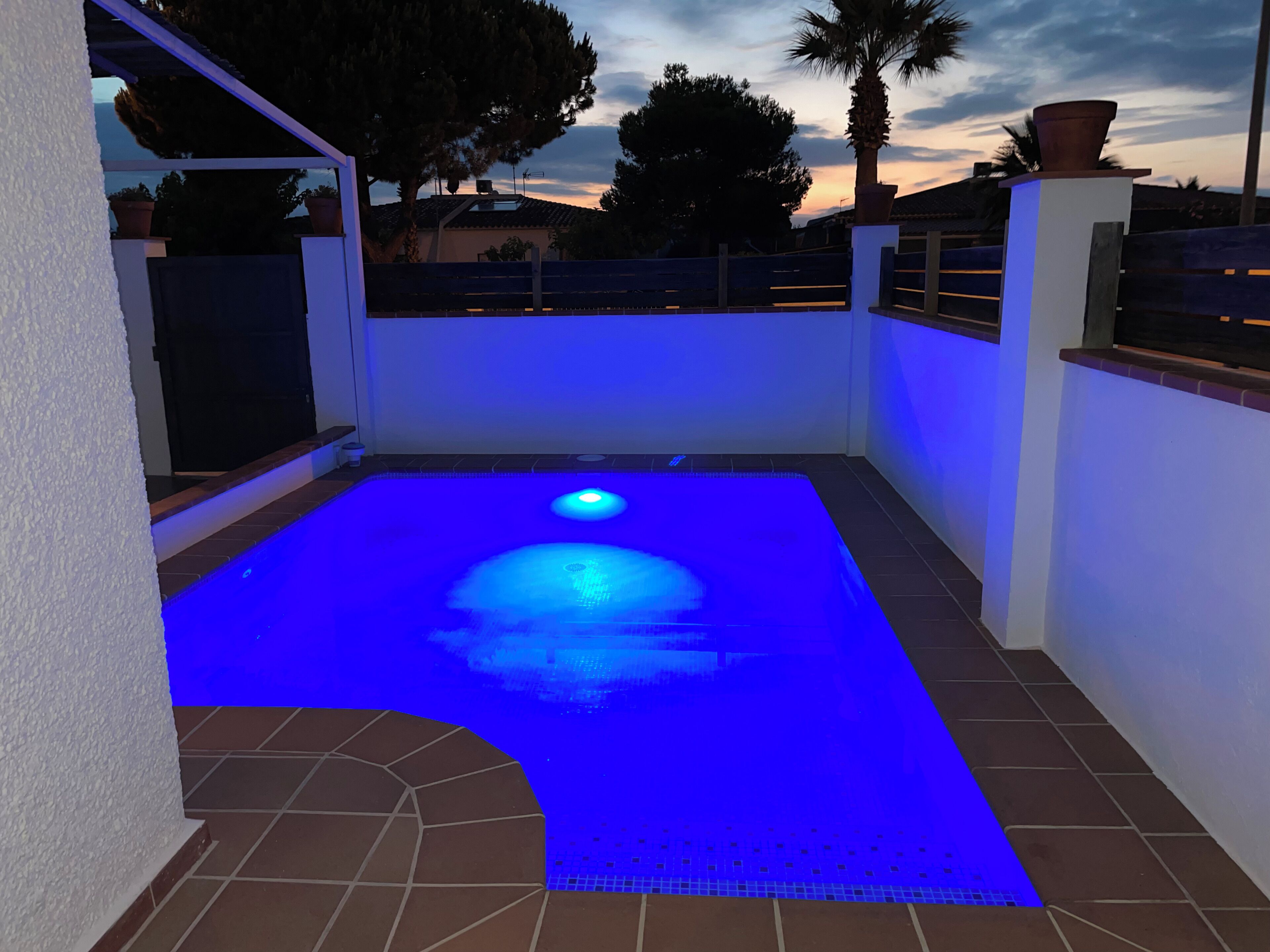 A swimming pool with blue lighting, surrounded by a white wall and a tiled floor.