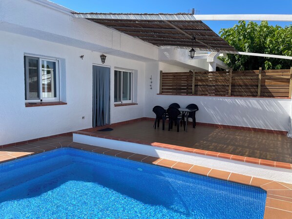 A swimming pool with a tiled edge, a patio with a table and chairs, and a covered area with a wooden roof. - Casa Rogi, with pool, ideal for family, on main street and near the beach (Riumar)