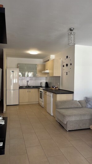 Eine kompakte Küche mit Kühlschrank, Herd und Spüle. Im Wohnbereich befindet sich ein Sofa und ein kleiner Tisch.