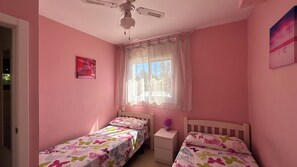 A bedroom with two single beds, a ceiling fan, a window with sheer curtains, and a small bedside table with a lamp. - Casa Rogi, with pool, ideal for family, on main street and near the beach (Riumar)