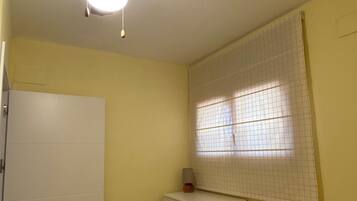 A room with a ceiling fan, a window with grid blinds, a white door, and a white dresser.