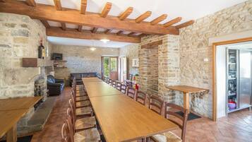 Un'ampia sala da pranzo con un lungo tavolo in legno e sedie, pareti in pietra e un camino in pietra.