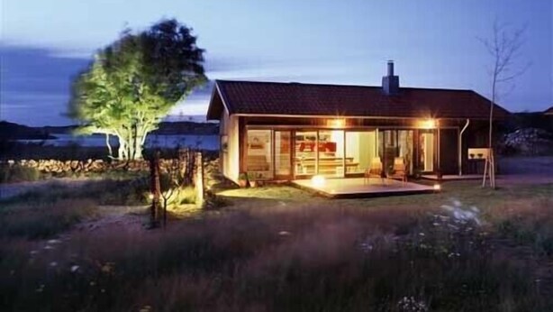 Ein modernes Haus mit großer Glasfront, rotem Dach und einer gut beleuchteten Veranda.