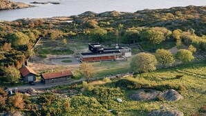 Ein modernes Haus mit rotem Dach, umgeben von üppiger grüner Landschaft und einem Gewässer.