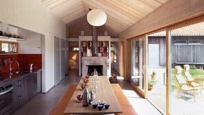 Eine moderne Küche mit einem langen Holztisch und Bänken, einem Kamin und einer großen Schiebeglastür zu einem Außenbereich.