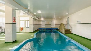 An indoor swimming pool with clear water, surrounded by tiled walls and a green artificial turf area. - Luxury Self Catering Lodge & Barn - Along NC500 - Indoor Private Swimming Pool (Latheronwheel)