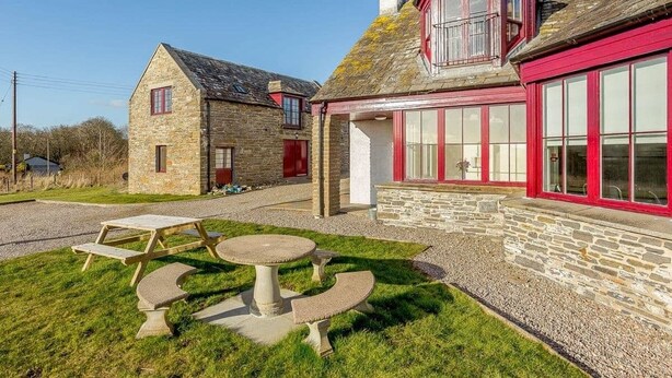 A stone building with a red door and windows, a stone bench, and a picnic table. - Luxury Self Catering Lodge & Barn - Along NC500 - Indoor Private Swimming Pool (Latheronwheel)