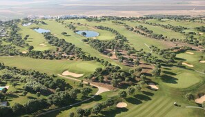 An aerial view of a golf course with multiple bunkers, water hazards, and trees.