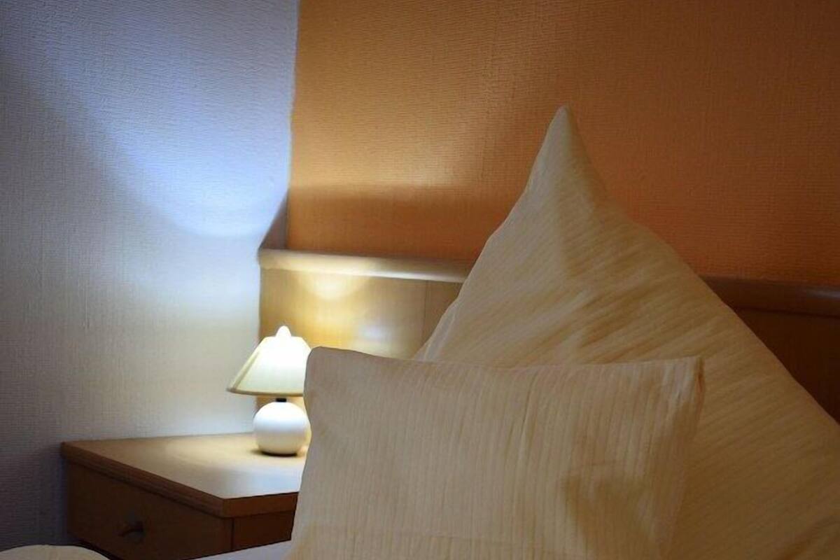 Un lit bien fait, avec un oreiller et une table de chevet sur laquelle se trouve une lampe.