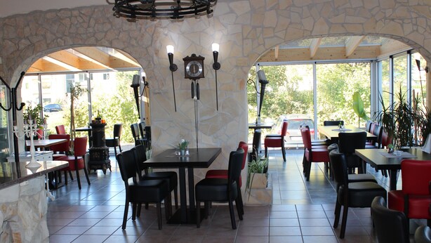 A restaurant with stone walls, multiple tables and chairs, and large windows allowing natural light. - Zum Goldenen Wagen (Maulburg)