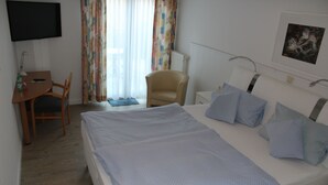 A hotel room with a large bed, a desk with a chair, a TV mounted on the wall, and a window with curtains. - Zum Goldenen Wagen (Maulburg)