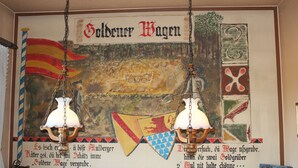 A wall with a historical banner and two hanging lamps. - Zum Goldenen Wagen (Maulburg)