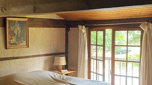 Una camera da letto con un letto grande, pavimento in legno, un quadro appeso al muro, un comodino con una lampada e una finestra con tende.