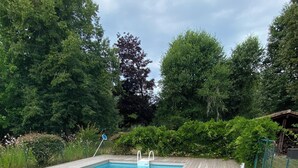 Un terrazzo in legno con piscina, immerso nel verde e con una struttura in legno sullo sfondo.