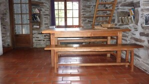 Una habitación rústica con una mesa y banco de madera, una escalera, una estantería y una ventana con vistas al verdor.