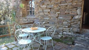 Un edificio de piedra con un muro de piedra y una ventana. Hay una mesa redonda con cuatro sillas y una cesta de fruta encima.