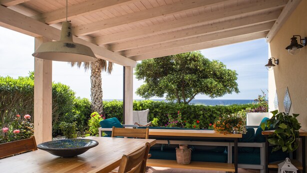 Une terrasse extérieure avec une table en bois, des bancs et une vue sur la mer.