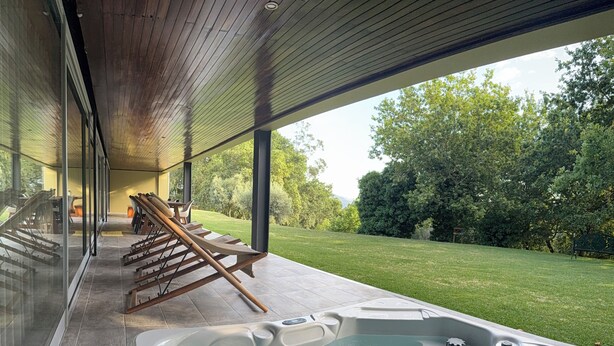 Un área moderna de hidromasaje al aire libre con terraza de madera y zona de estar cubierta con vidrio.