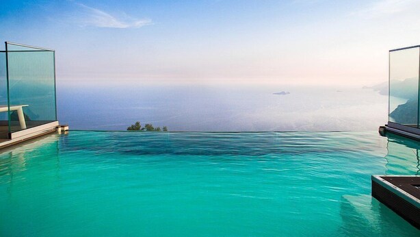 Una piscina infinita con agua azul cristalina y vistas al océano y a la costa distante.