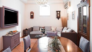 Una sala de estar con televisor, sofás, una mesa de comedor y una araña.