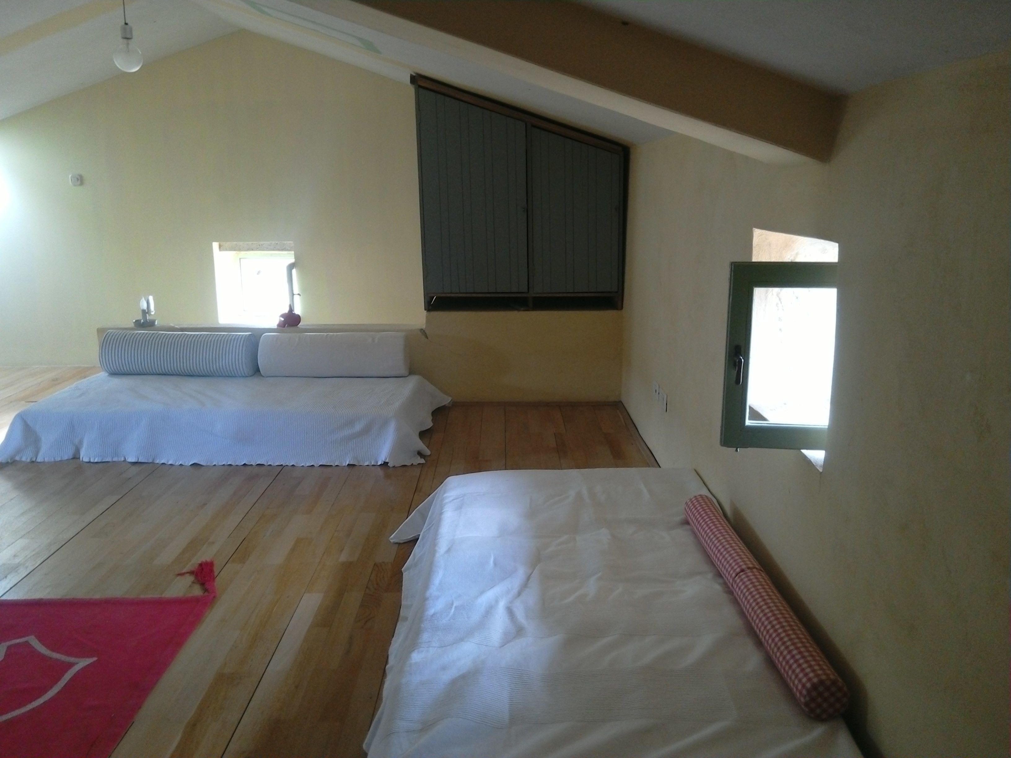A bedroom with two beds, wooden flooring, a window, and a ceiling light.