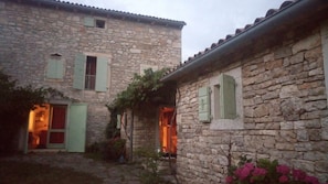 Un bâtiment en pierre avec deux portes et fenêtres apparentes, dont l’une est dotée d’un volet vert.