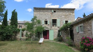 A stone building with a red door, a balcony, and a grassy yard with a chair. - Holiday Home Augusta (Zminj)
