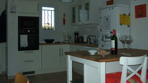 Une cuisine avec des meubles blancs, un plan de travail en bois, un réfrigérateur, une machine à café et une bouteille de vin.