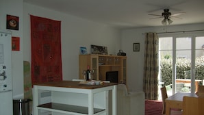 Un espace de vie compact comprenant un coin repas, un comptoir de cuisine, un meuble en bois et une porte-fenêtre coulissante donnant sur un espace extérieur.