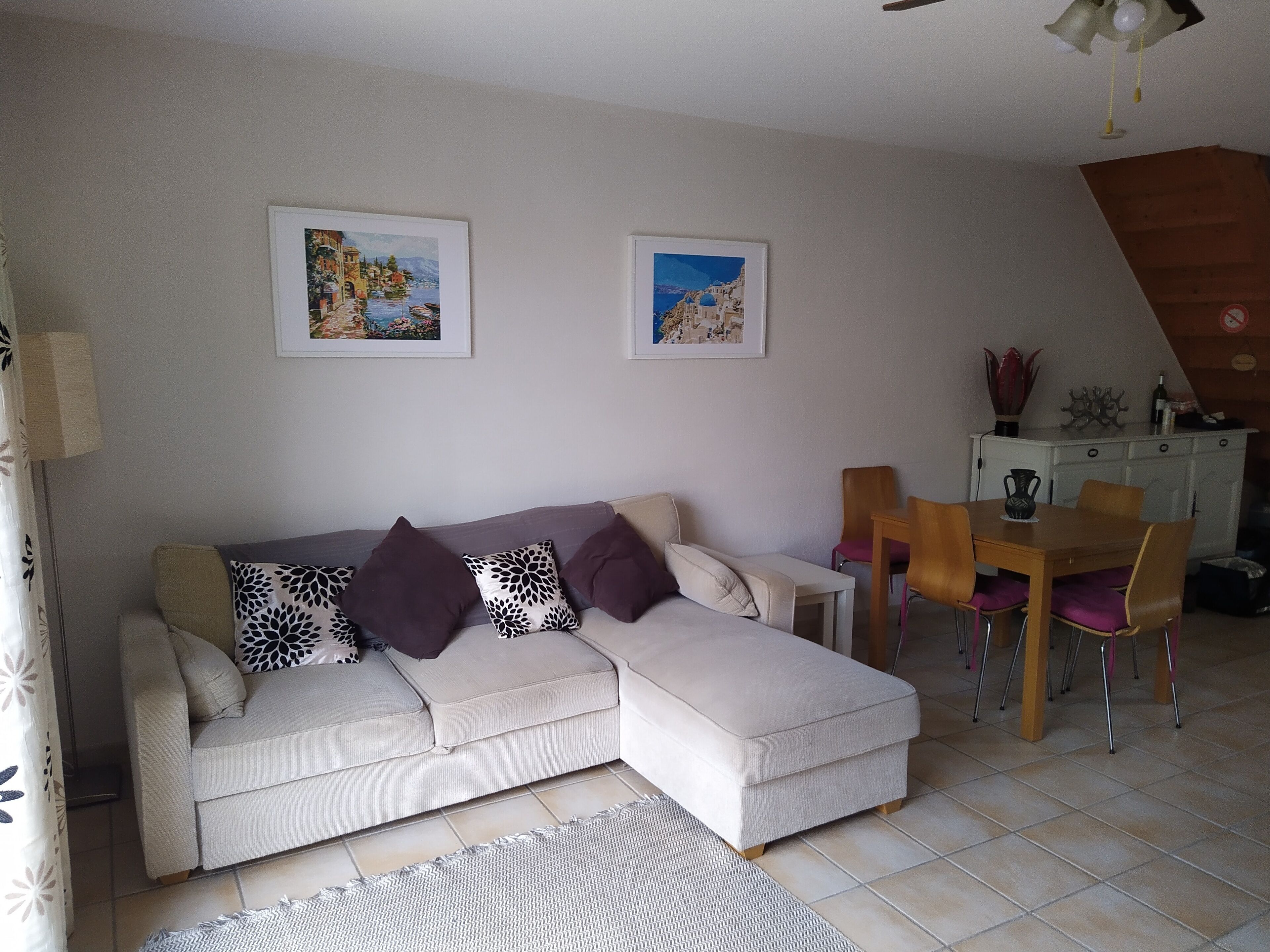 A living room with a sofa, a dining table with chairs, and two framed pictures on the wall.