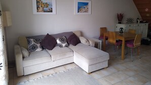 Un salon comprenant un canapé, une table à manger avec des chaises et deux tableaux encadrés accrochés au mur.