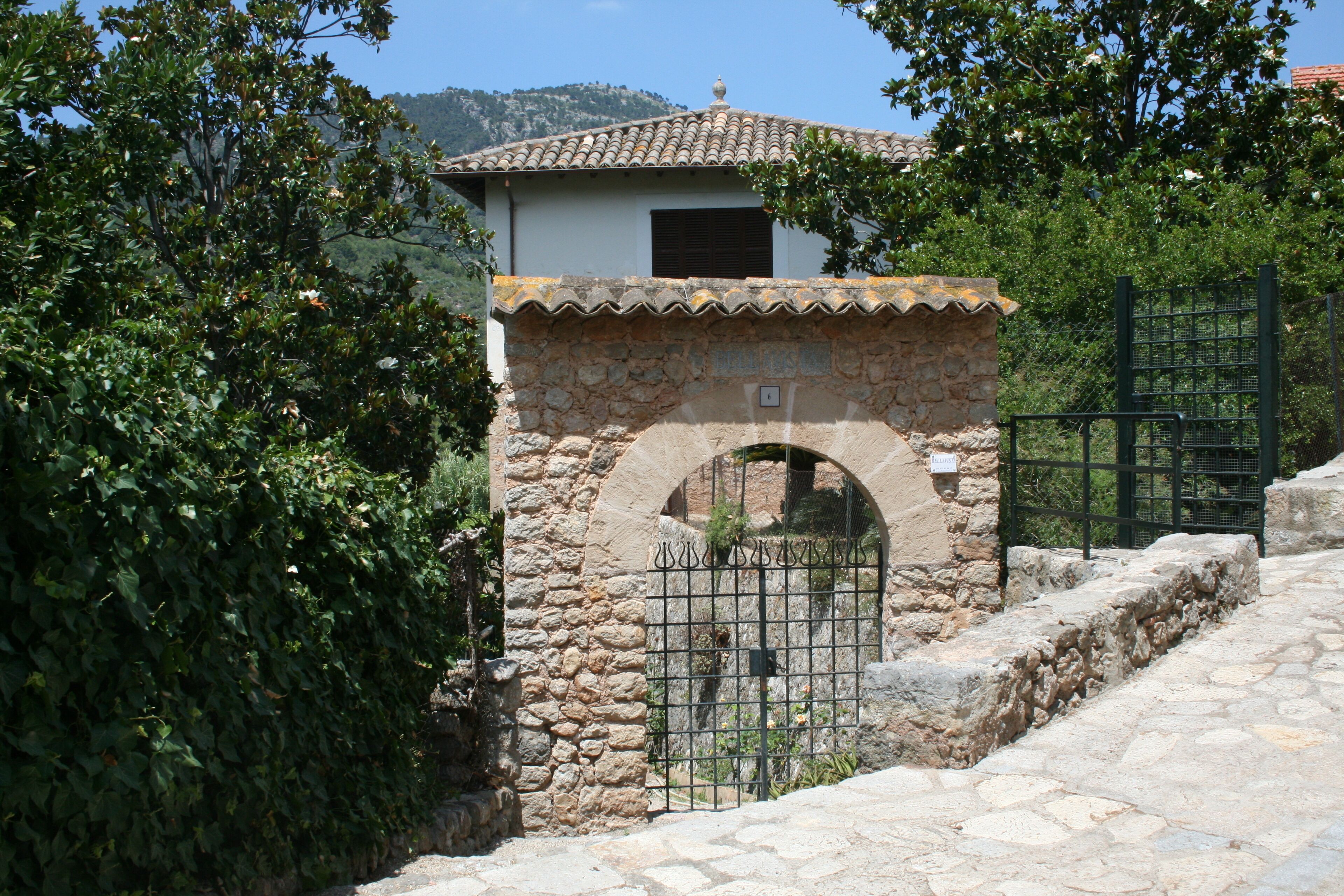 A stone building with a tiled roof, a metal gate, and a stone wall with a circular opening.