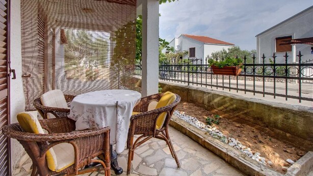 Eine Terrasse mit Korbmöbeln und einem Tisch, mit Blick auf eine Straße mit Häusern und einem Zaun.