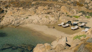 Ein felsiger Strand mit klarem, flachem Wasser und mehreren Liegen mit Sonnenschirmen.