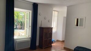 Une chambre à coucher avec un lit, une fenêtre avec des rideaux, un radiateur, une armoire en bois et un petit tabouret.