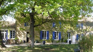 Un bâtiment en pierre avec des volets bleus, une table à manger et un chien dans un jardin.