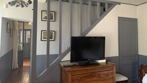 Un escalier, une télévision posée sur une commode en bois, des tableaux encadrés accrochés au mur et une porte.