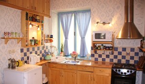 A kitchen with wooden cabinets, a microwave, a stove, and a window with checkered curtains. - Serbian Village Farmhouse (Stara Moravica)