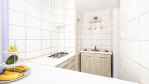 A compact kitchen with white tiles, a gas stove, a sink, and wooden cabinets.