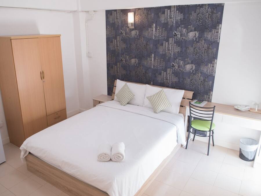 Un dormitorio ordenado con cama, un armario de madera, un escritorio con silla y pared con diseño.