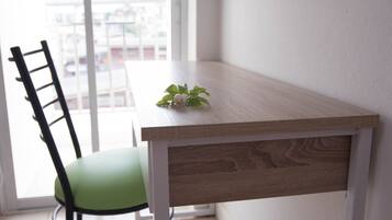 A corner of a room with a wooden table, a green chair, and a view of buildings through a window.