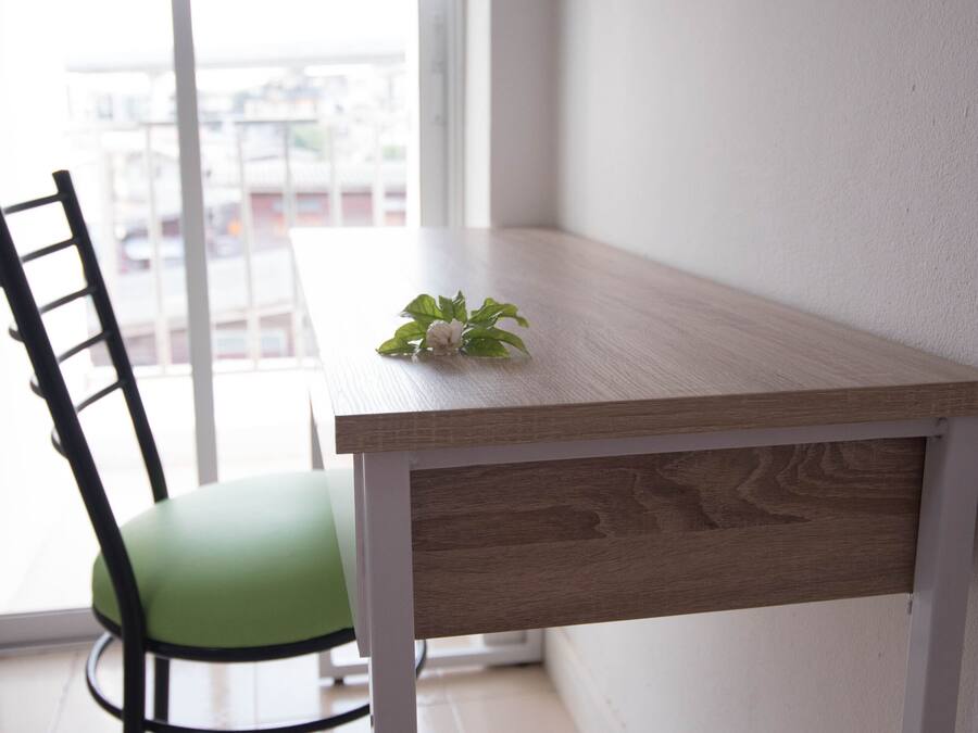 A corner of a room with a wooden table, a green chair, and a view of buildings through a window.