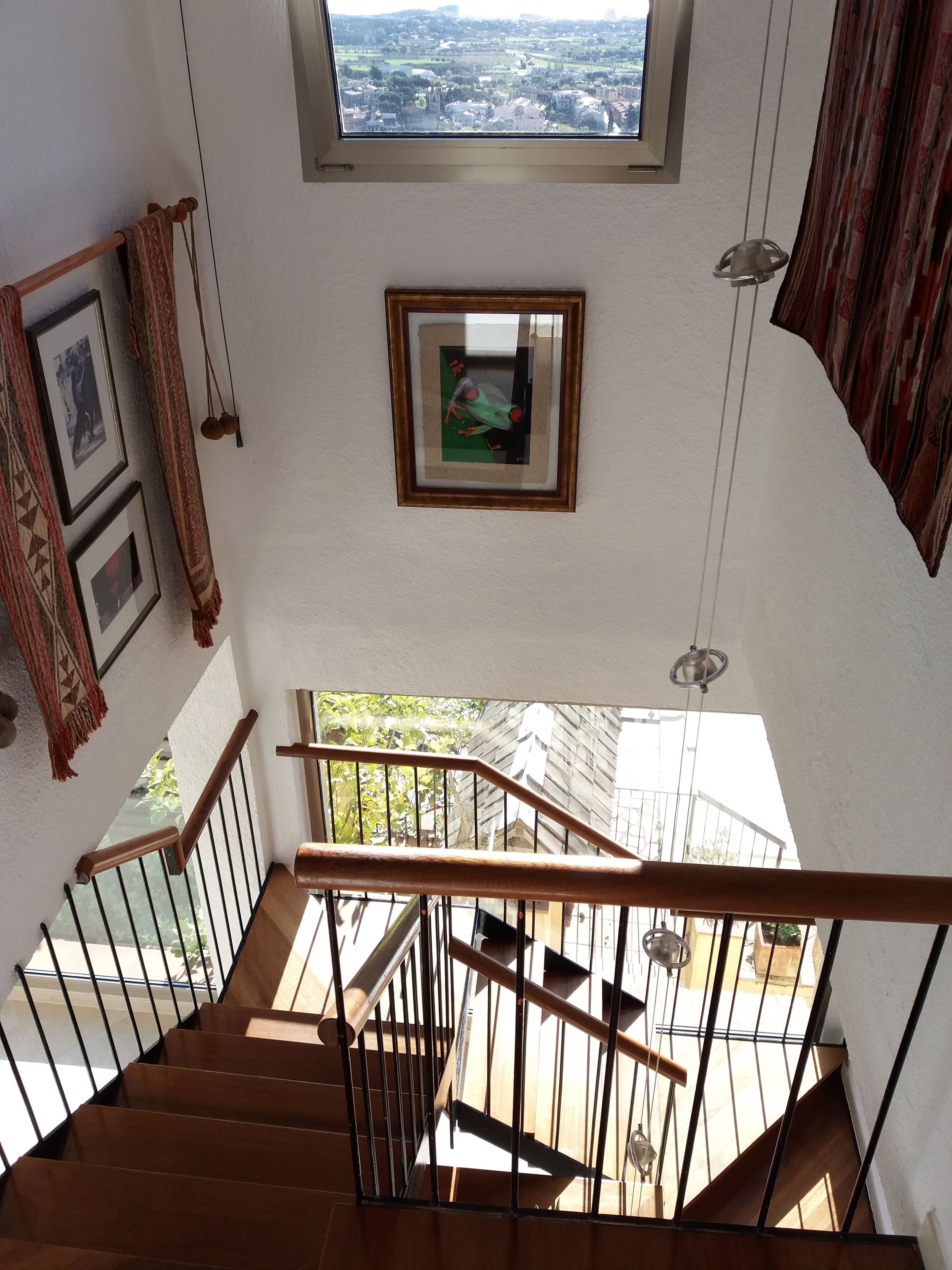 Un escalier avec des rampes en bois et des balustrades en métal, menant à un balcon d’où l’on peut admirer la vue sur la ville.