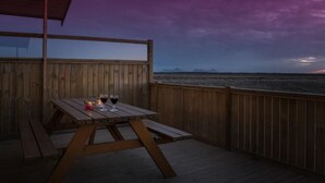 A wooden deck with a table and benches, overlooking a beach at dusk. - Bryggjur (Rangárþing eystra)